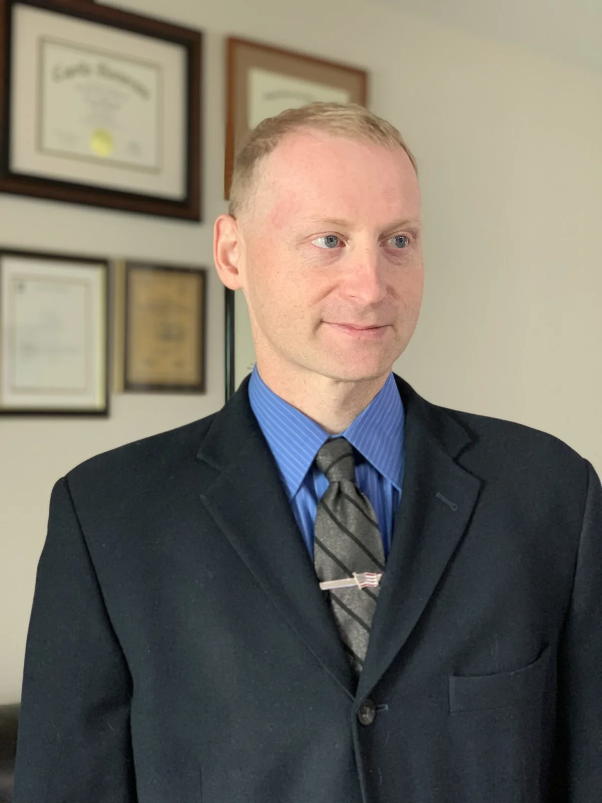 Dr. George Ackerman in a suit and tie, photographed in front of his framed diplomas